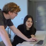 Two colleagues strategize on a laptop, focusing on the 'four sales velocity levers' to boost sales efficiency and drive business growth.